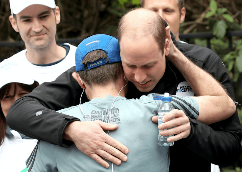Prince Harry hugs a marathon runner while giving him a water bottle.