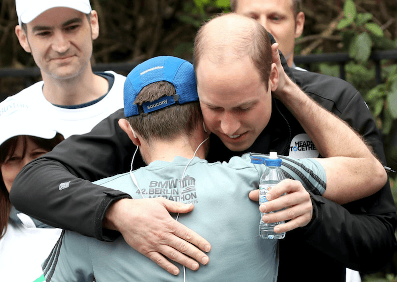 Prince Harry hugs a marathon runner while giving him a water bottle. Prince Harry hugs a marathon runner while giving him a water bottle.