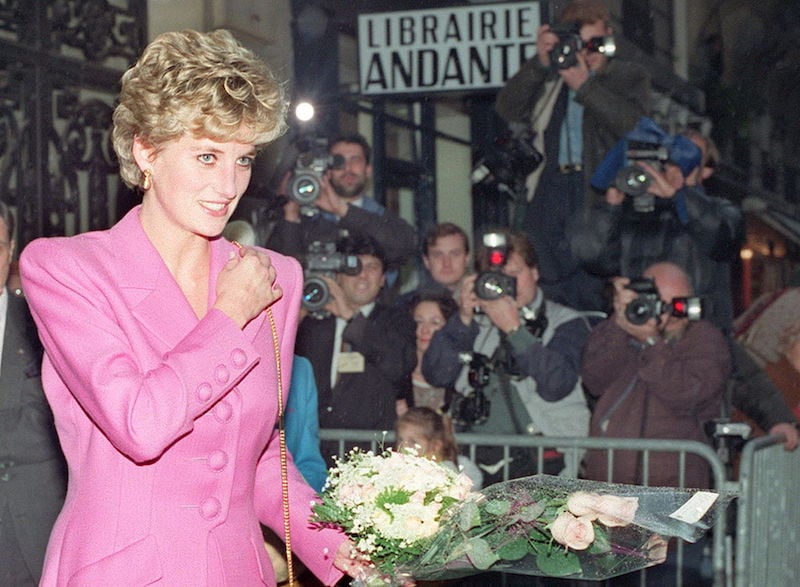 Princess Diana wears a pink suit and holds flowers while getting photographed.