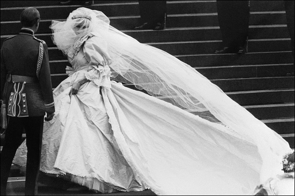 A black and white photo of Princess Diana walking up the stairs in her famous wedding gown. A black and white photo of Princess Diana walking up the stairs in her famous wedding gown.