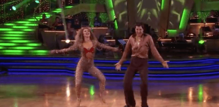 Ralph Macchio and Karina Smirnoff dancing while wearing brown outfits. 