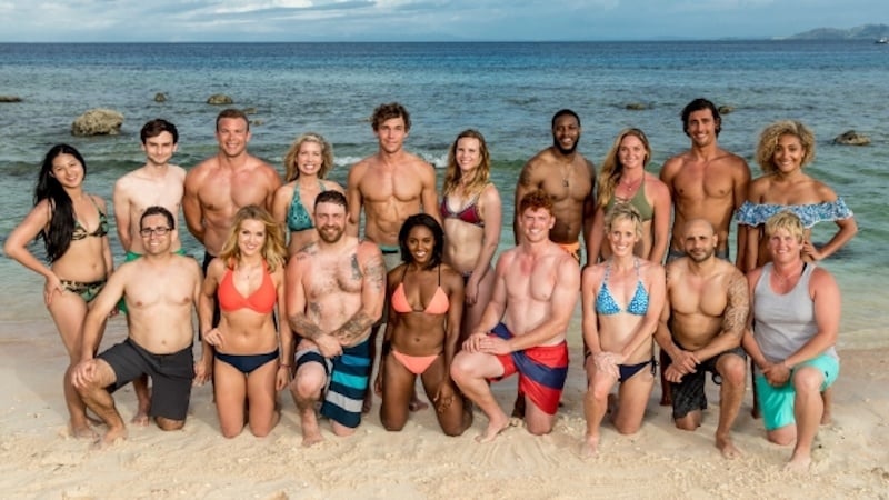 A group of people pose in front of the ocean on a beach in bathing suits