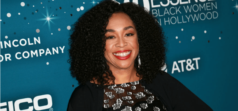Shonda Rhimes smiles while posing on the red carpet in a black dress.