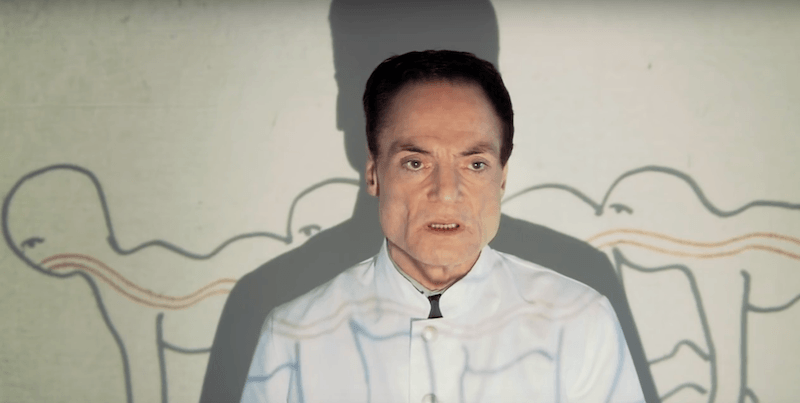 The Human Centipede's Dr. Josef Heiter stands in front of a projection screen The Human Centipede's Dr. Josef Heiter stands in front of a projection screen