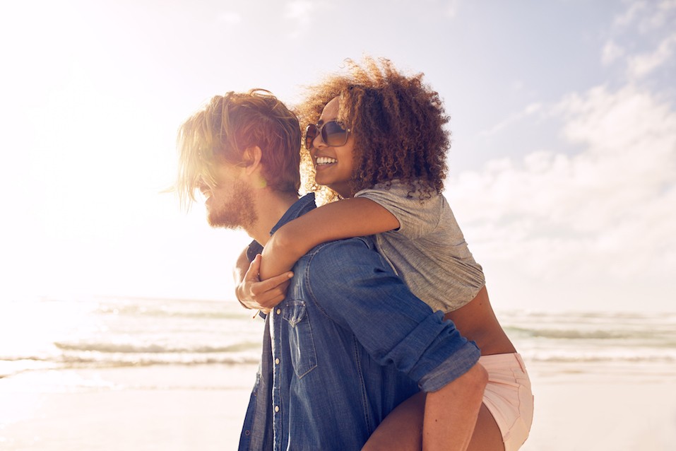 young man carrying his girlfriend on his back at the beach