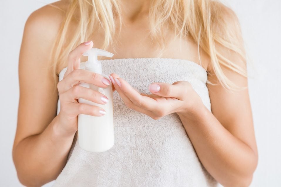 Young woman in towel after shower using body cream
