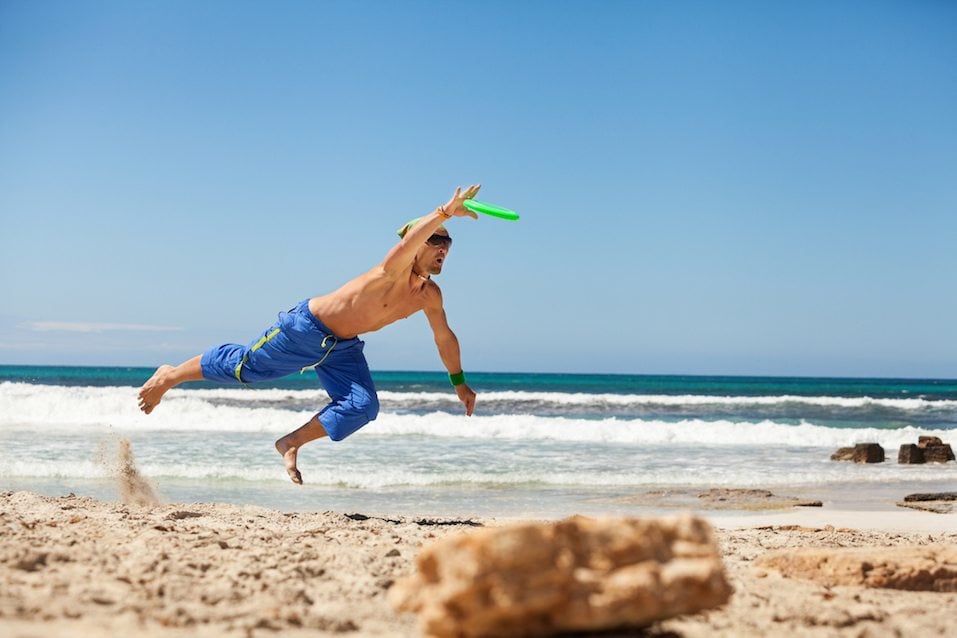 attractive man playing frisby on beach in summer