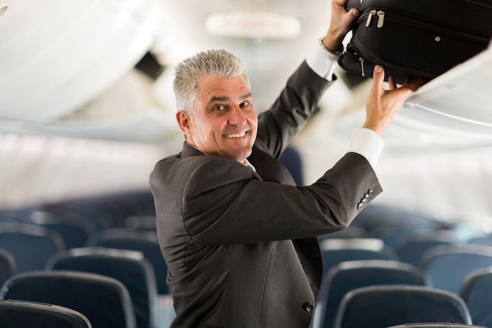 business traveler putting luggage into overhead locker on airplane