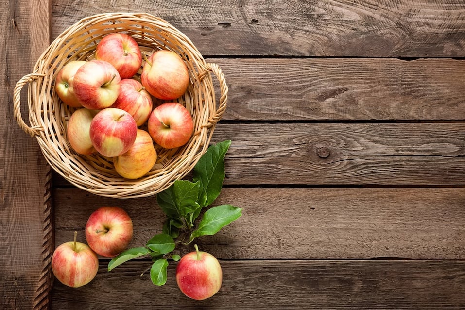 fresh apples in wicker basket on wooden table