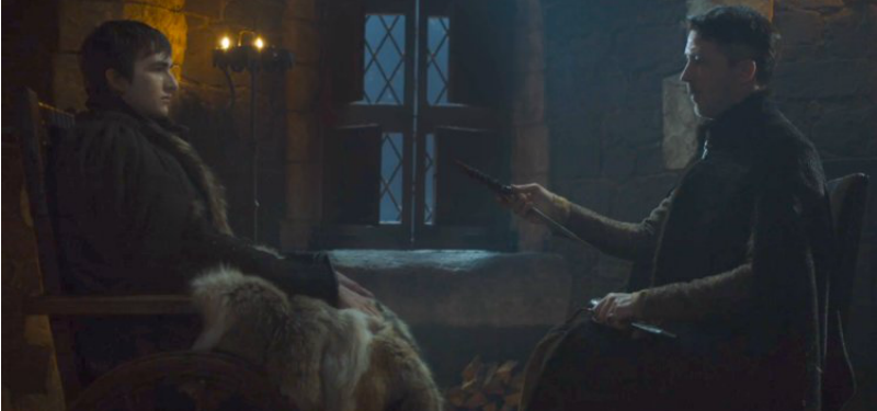 Bran and Littlefinger are seated across from each other and Littlefinger is handing Bran a dagger. Bran and Littlefinger are seated across from each other and Littlefinger is handing Bran a dagger.
