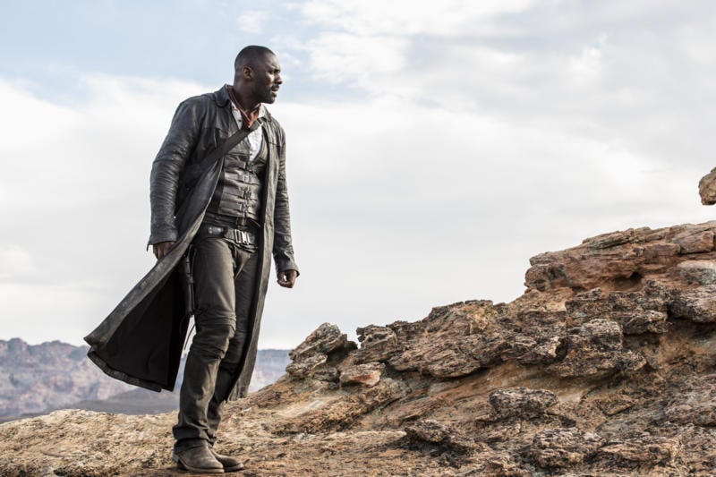 Idris Elba in a black leather duster looking out over rocks