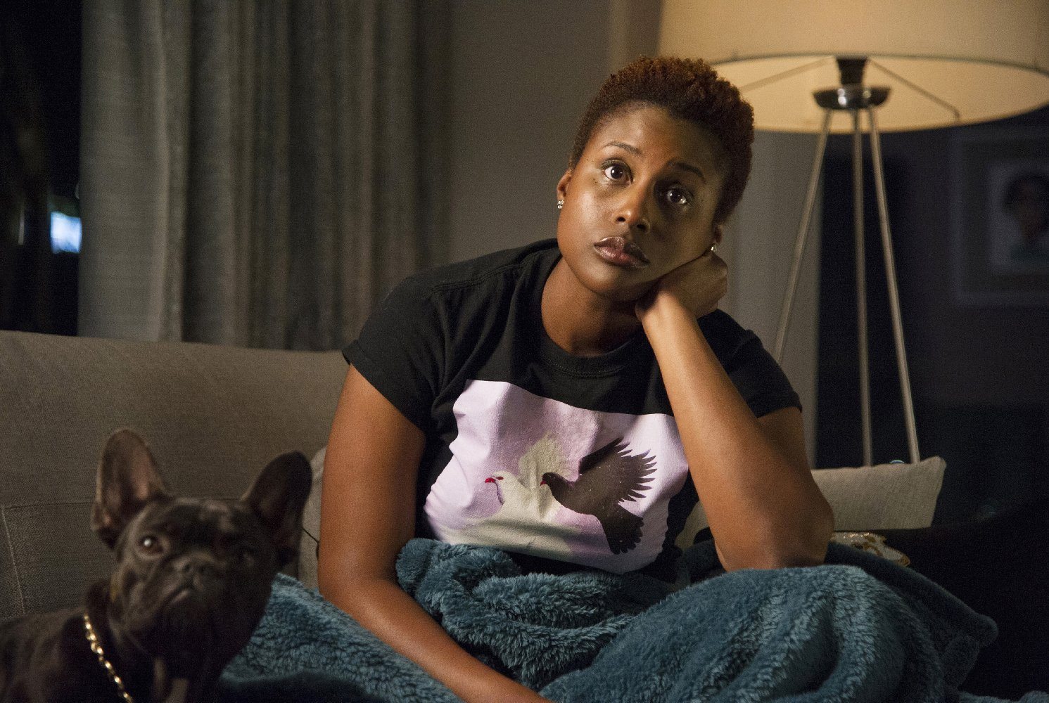 Issa Rae with her head resting on her hand sitting on a couch next to a French Bull Dog