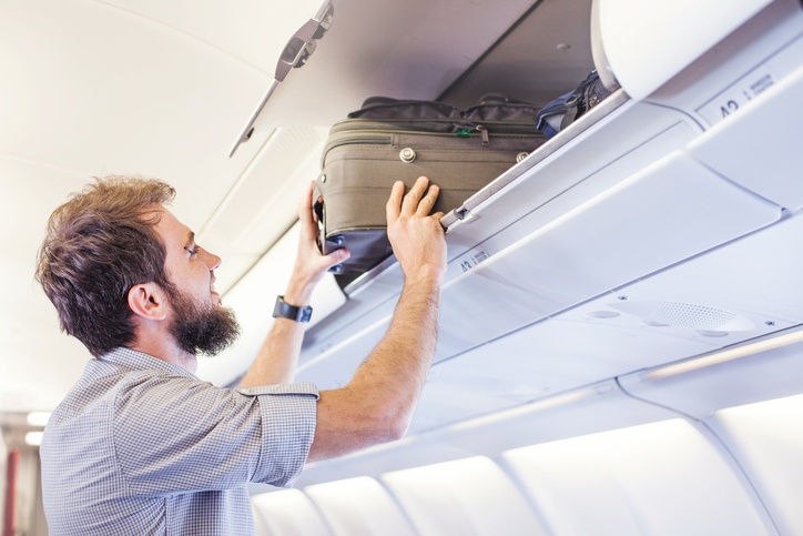 man putting luggage on the top shelf on airplane