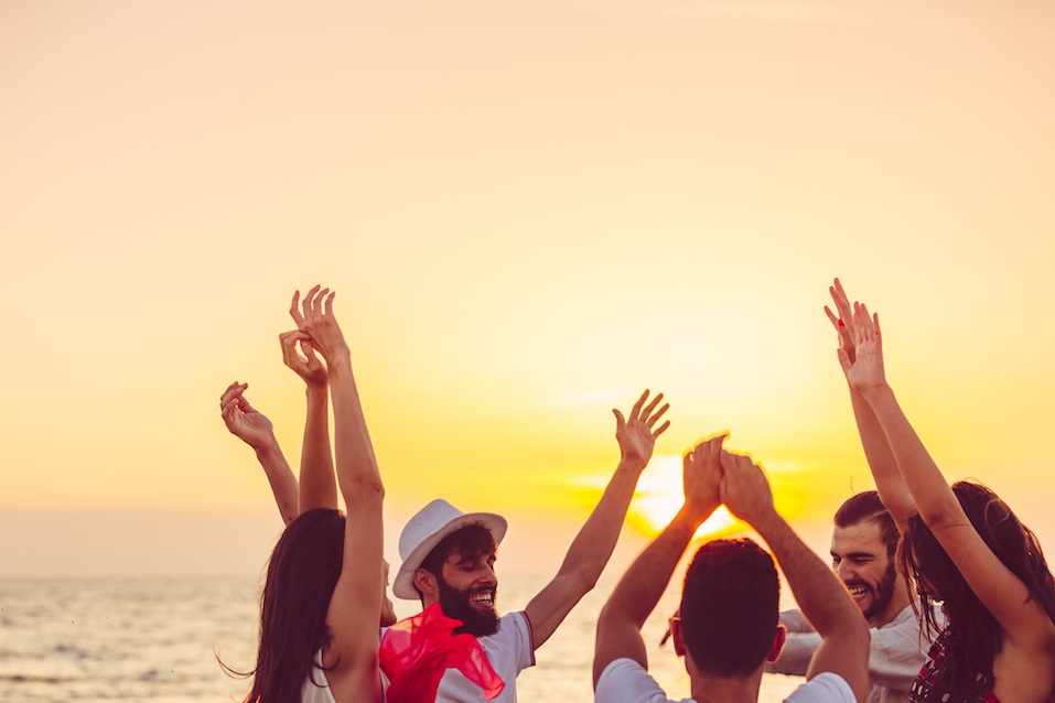 people dancing at the beach with hands up