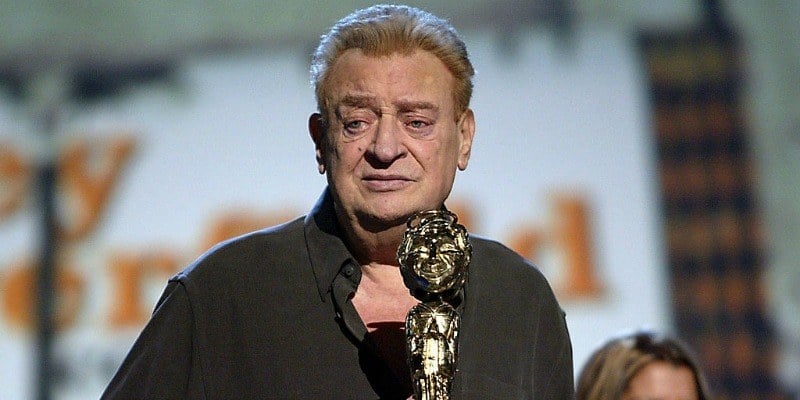 Rodney Dangerfield is on stage with an award.