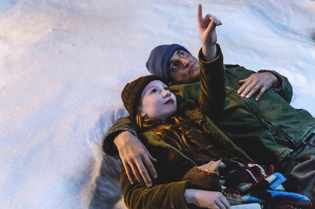 A child and her father lay in the snow as she points up at the sky A child and her father lay in the snow as she points up at the sky