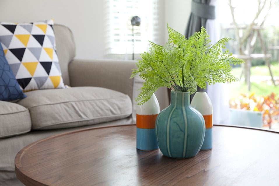 bunte Vase mit Blume auf Holztisch und Sofa im Wohnzimmer