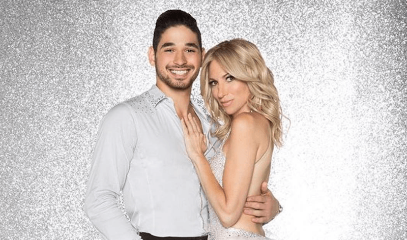 Alan Bersten and Debbie Gibson standing with each other in front of a glittery gray background.