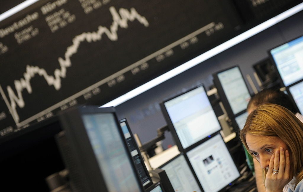 A stock broker sits in front of a board displaying German share index DAX