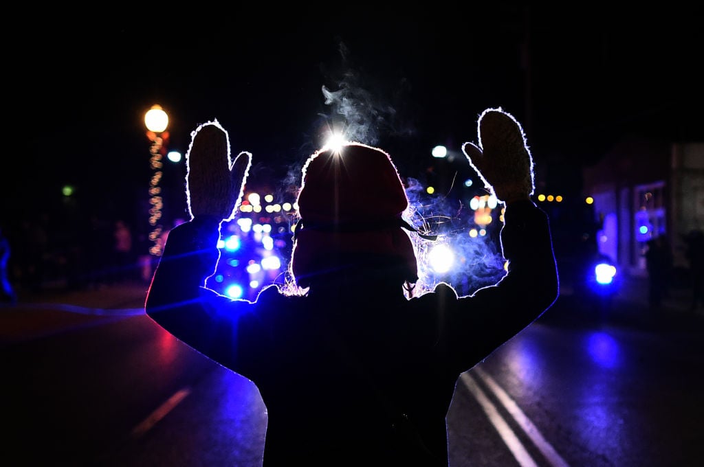 A woman holds her hands up in front of a police car