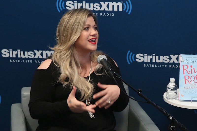 Kelly Clarkson gestures with her hands while talking into a microphone
