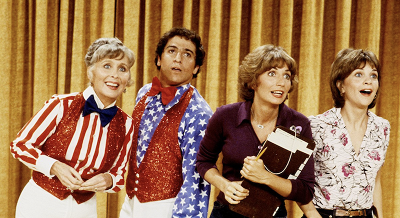 Laverne, Shirley, Edna and Carmine standing on a stage while looking outwards.