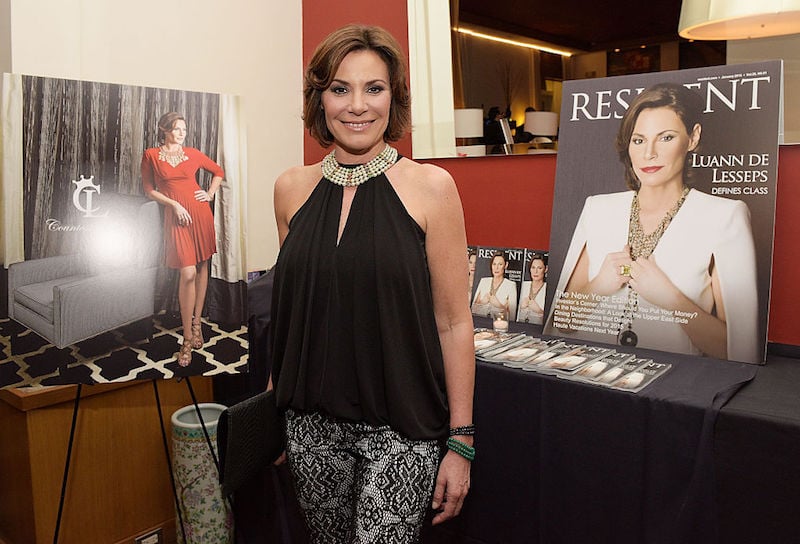 Luann de Lesseps posing in front of a table and photos of herself. Luann de Lesseps posing in front of a table and photos of herself.