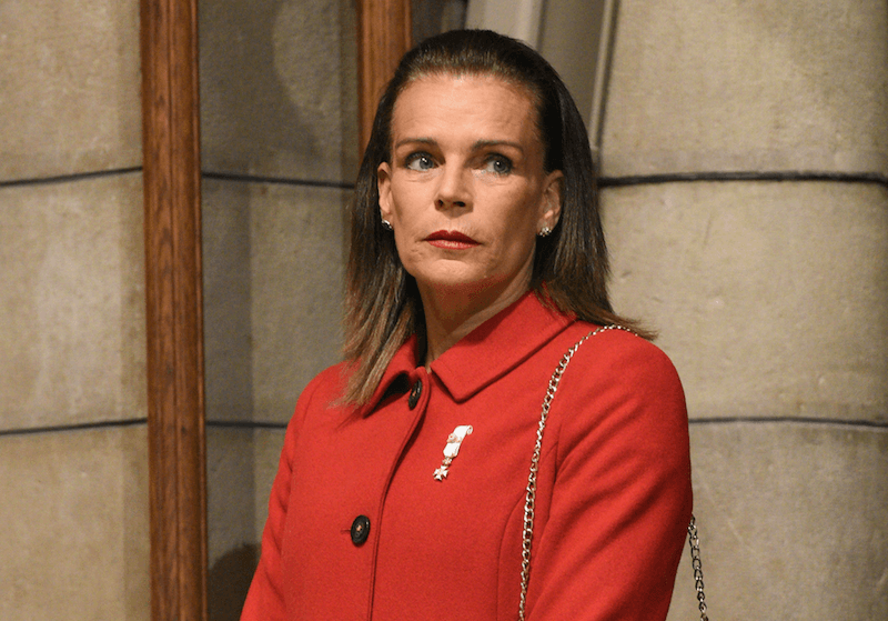 Princess Stephanie of Monaco stands in front of a building wearing an orange coat. Princess Stephanie of Monaco stands in front of a building wearing an orange coat.
