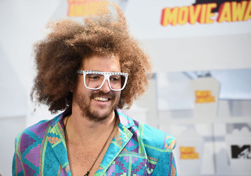 Redfoo smiles while wearing a a colorful suit and white glasses.
