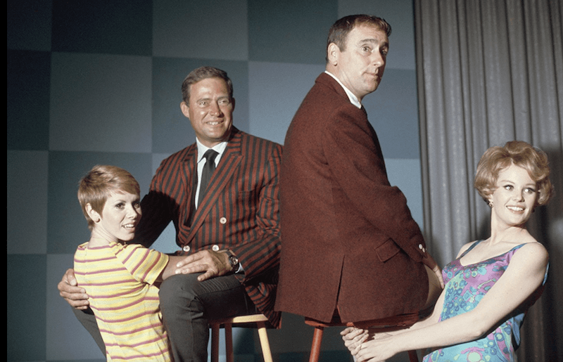 Two men sit on stools on stage while two women sit in the ground in front of them Two men sit on stools on stage while two women sit in the ground in front of them