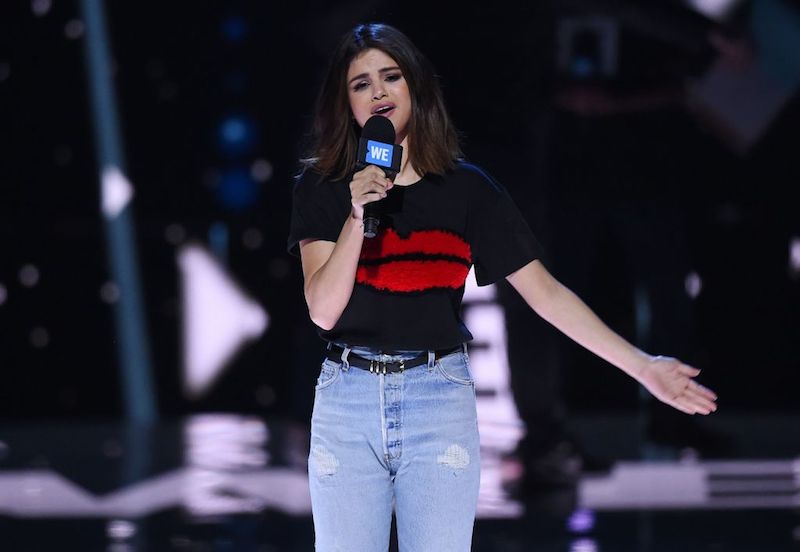 Selena Gomez performs while holding a mic and extending one arm. Selena Gomez performs while holding a mic and extending one arm.