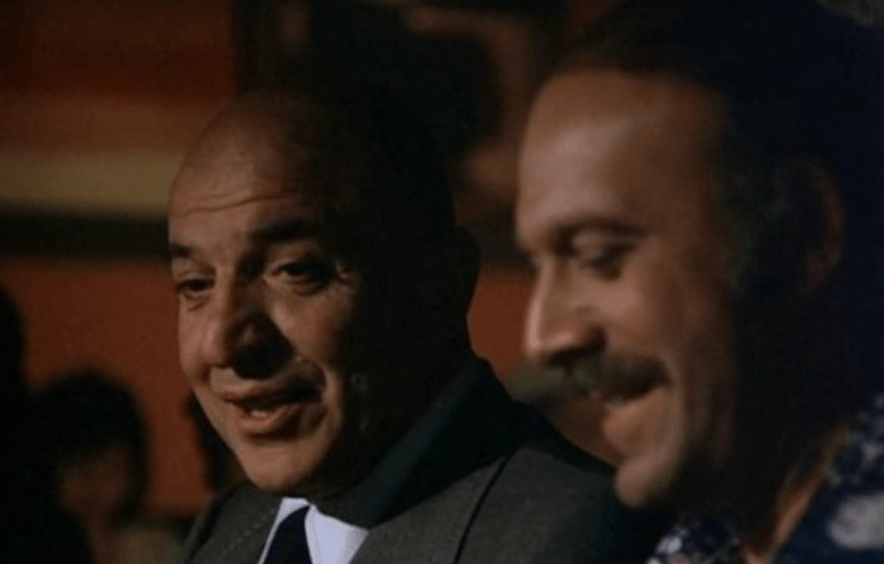 Telly Savalas turning to the side and talking to another person. Telly Savalas turning to the side and talking to another person.