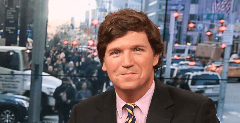 Tucker Carlson smiling while wearing a black suit and striped tie. 