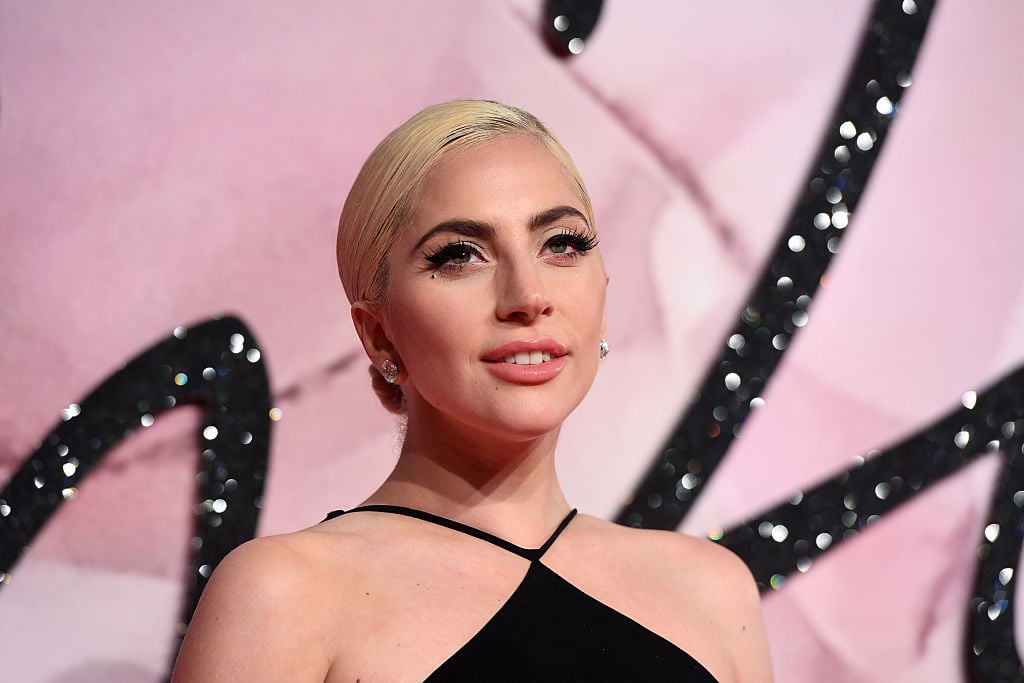 Lady Gaga smiles as she poses in front of a pink and black sequined background. 