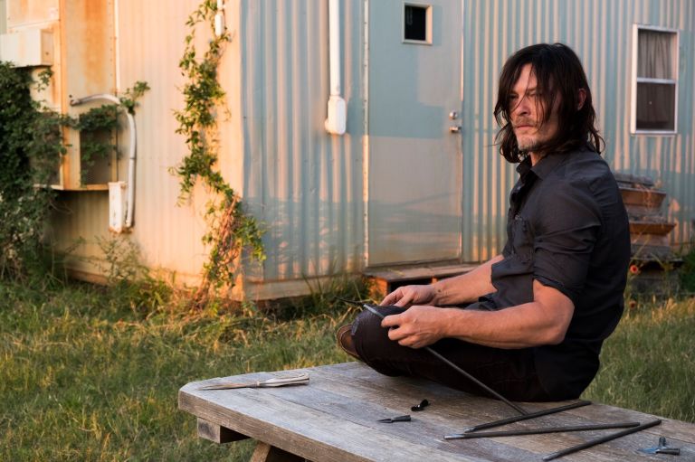 Daryl sits on a bench in front of a trailer holding a tool Daryl sits on a bench in front of a trailer holding a tool