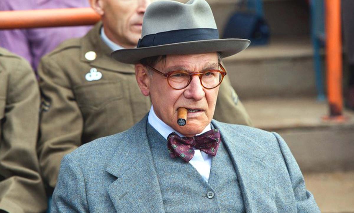 Harrison Ford wears a suit and fedora and smokes a cigar as Branch Rickey in 42