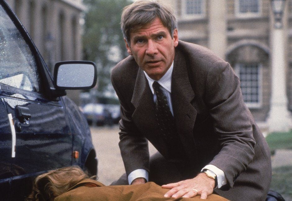 Harrison Ford crouches near a car in a suit as Jack Ryan in Patriot Games
