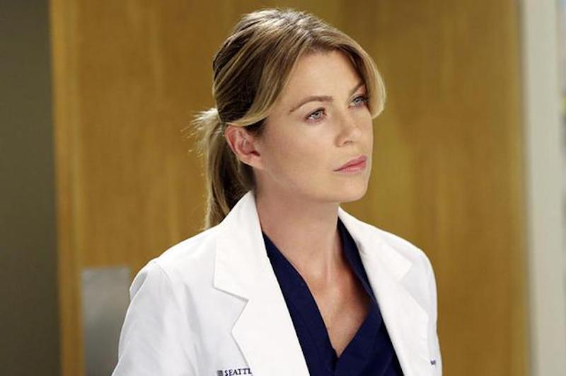 Meredith Grey stands in a white doctors coat and looks ahead