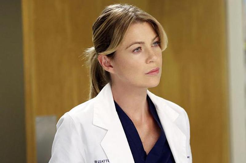 Meredith Grey stands in a white doctor's coat and looks ahead