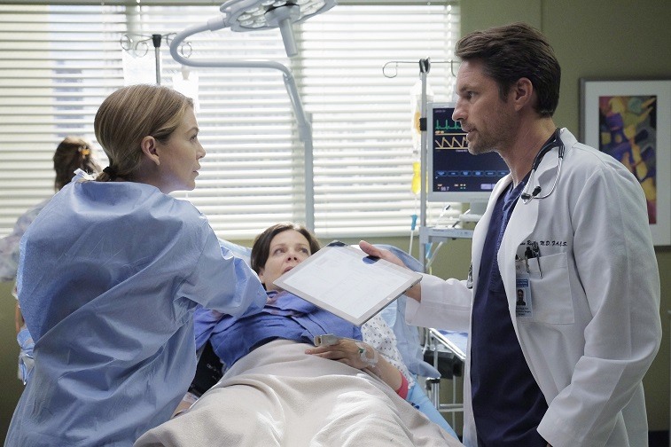 Meredith and Riggs in a patient's room working together on Grey's Anatomy