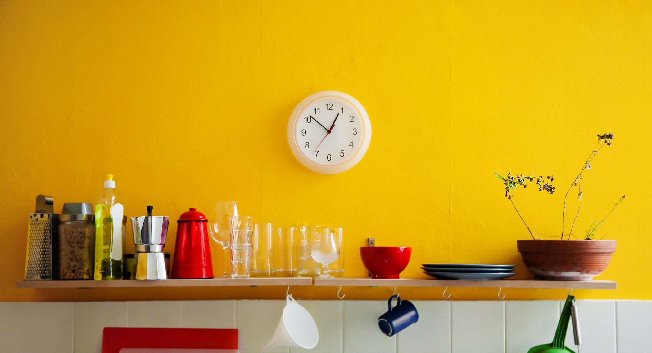 Yellow wall in kitchen with shelf and clock
