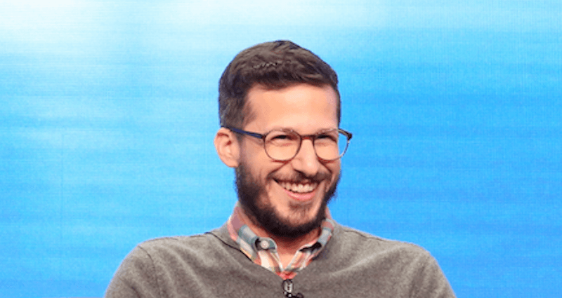 Andy Samberg laughing in front of a blue screen