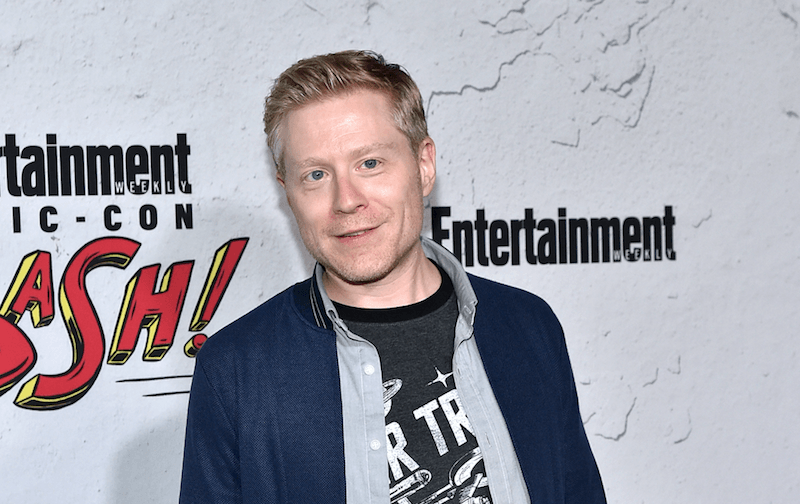 Anthony Rapp smiling and standing on a red carpet.