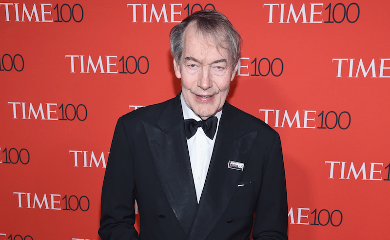 Charlie Rose stands and smiles in a black tuxedo while standing on a red carpet. Charlie Rose stands and smiles in a black tuxedo while standing on a red carpet.