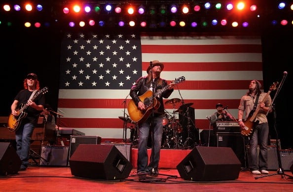 Kid Rock playing guitar against an American flag background 