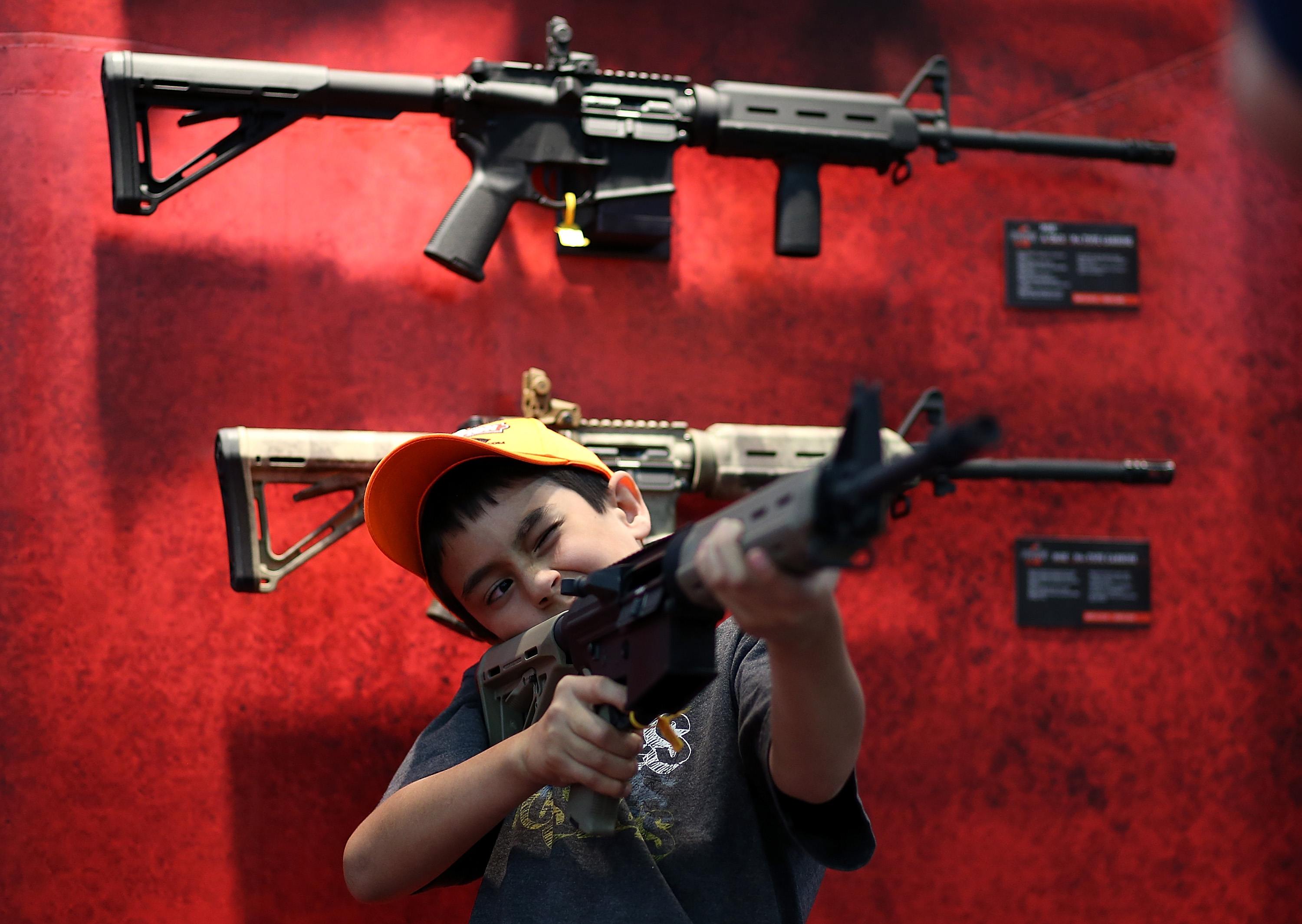 a child tries out an assault rifle against a red display with guns