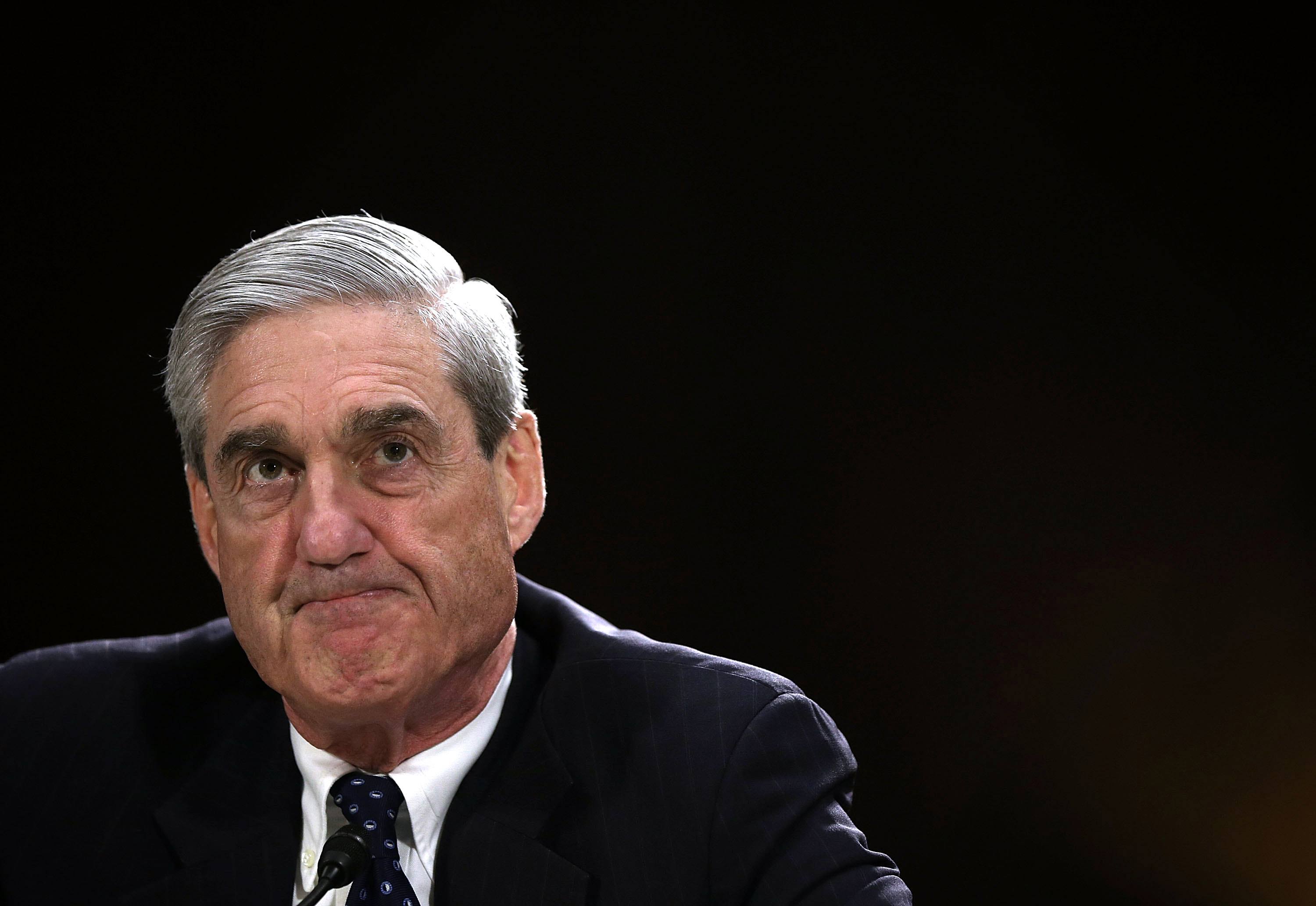 Robert Mueller in a dark suit and a dark tie against a black background Robert Mueller in a dark suit and a dark tie against a black background