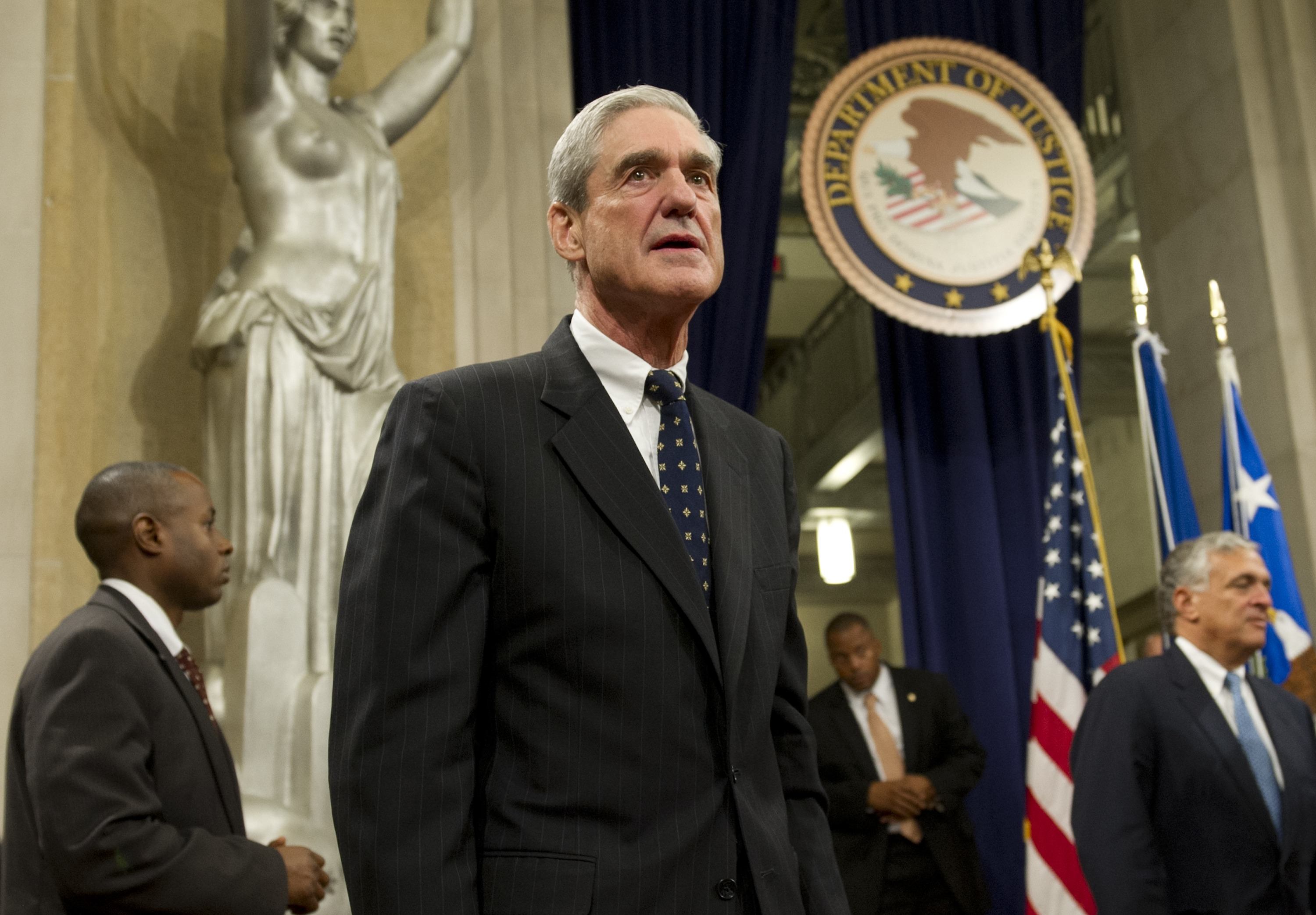 Robert Mueller standing in front of a statue of lady justice and the seal of the Department of Justice.
