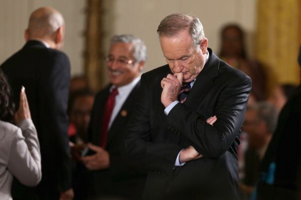 Bill O'Reilly in a dark suit looking thoughtful, surrounded by people
