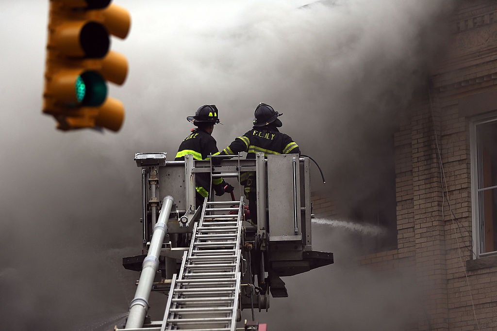 firefighters on a ladder in front of a building with smoke firefighters on a ladder in front of a building with smoke